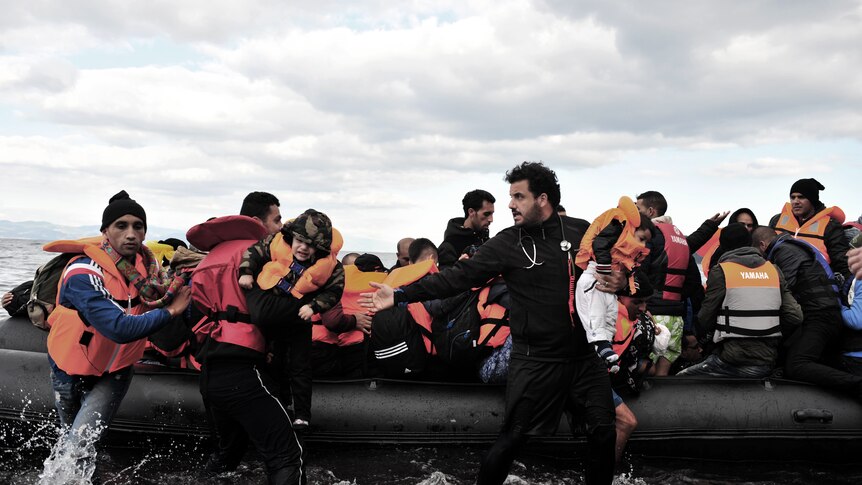 A man helps refugees out of a boat and onto dry land.