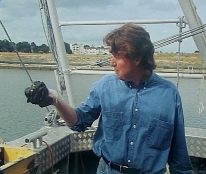 Mr Hogarth with his sleeves rolled up looks at his hand holding greasy toxic sludge while on a boat in the bay.