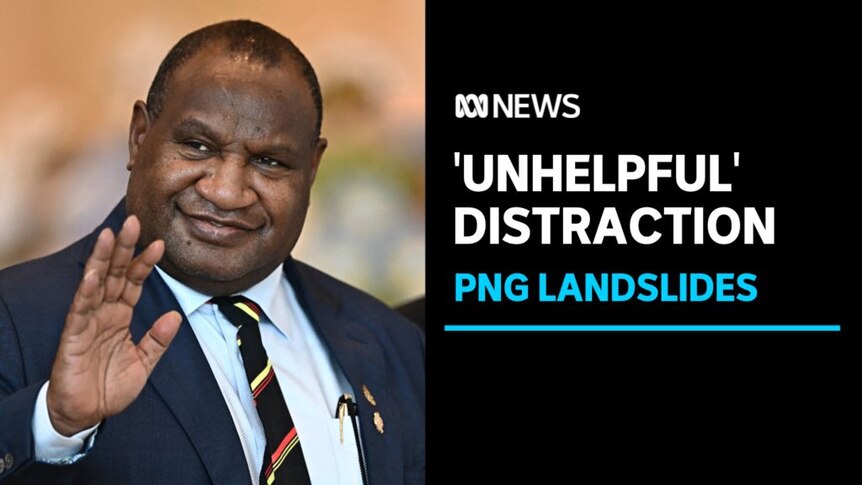'Unhelpful' Distraction, PNG Landslides: A man in a blue suit and colourful tie waves to someone off camera.