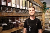 A man wearing an apron stands in a store selling whole foods, nuts and beans etc.