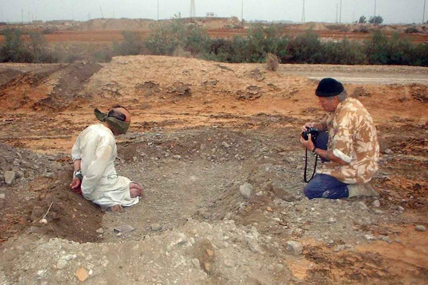 Sebastian Rich kneels in the dirt taking a photo of an Iraq prisoner of war