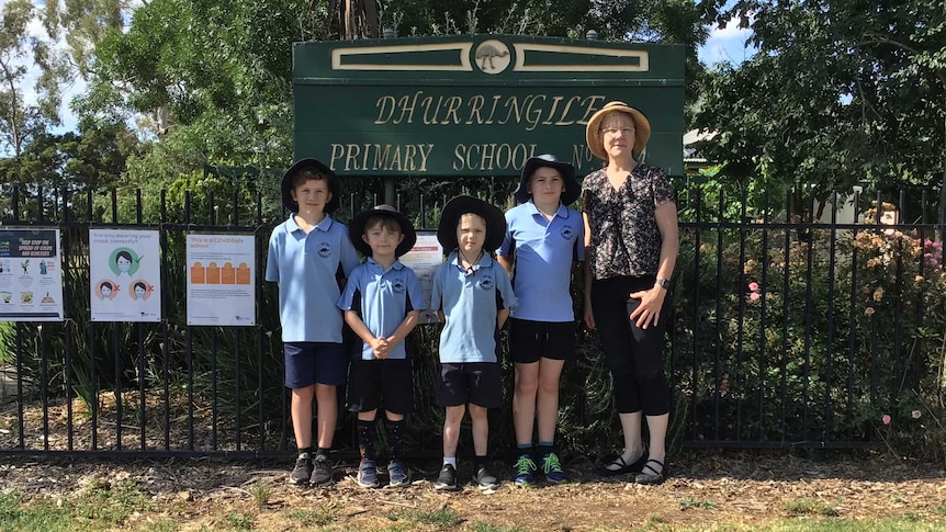 four young children and woman stand side by side in front of school sign