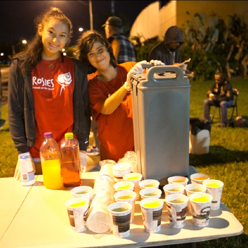 Two young ladies standing behind a table covered with cups of juice or cordial