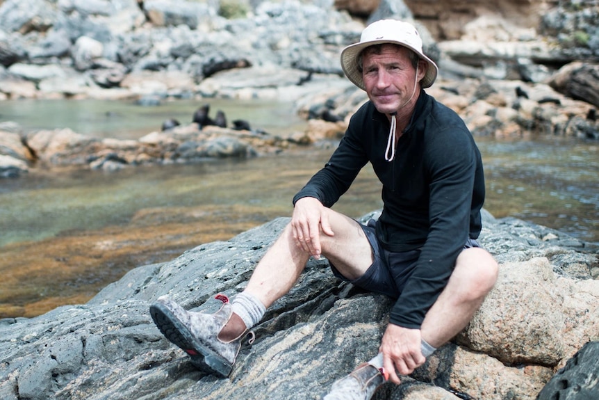 He sits on a rock in a drawstring hat and boots