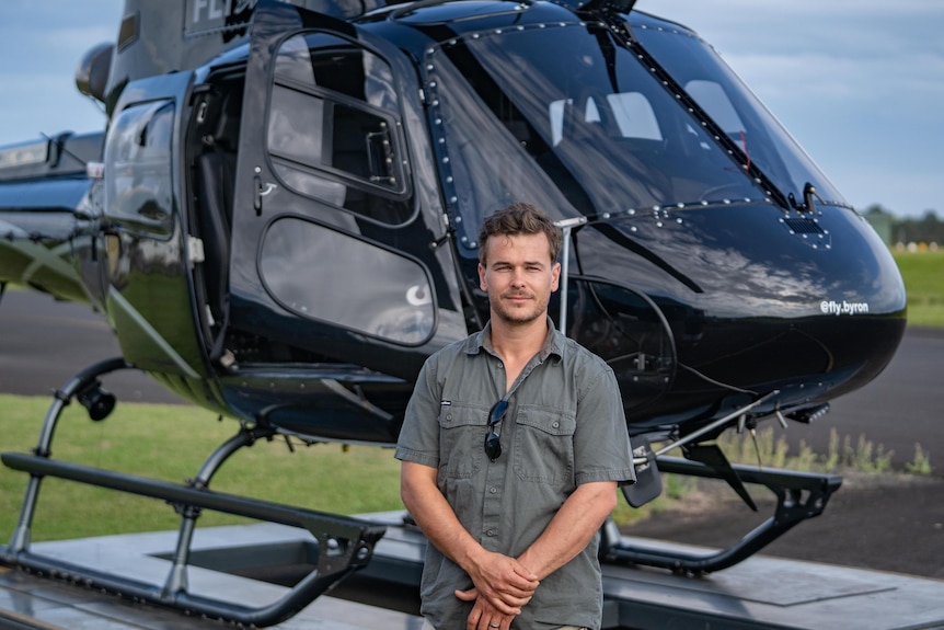 A man in a grey shirt standing in front of a small black helicopter