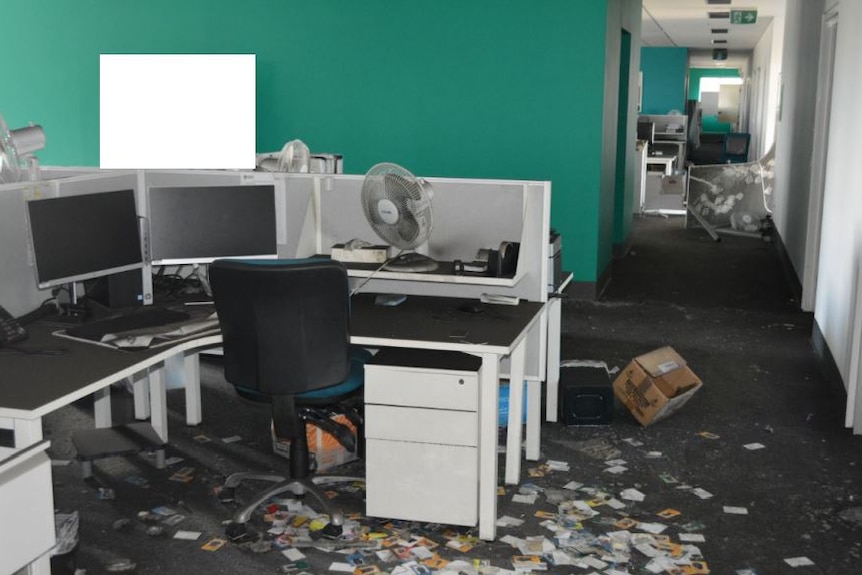 A desk and chair in an office, with object strewn across the floor.