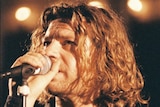 Michael Hutchence stands holds a microphone