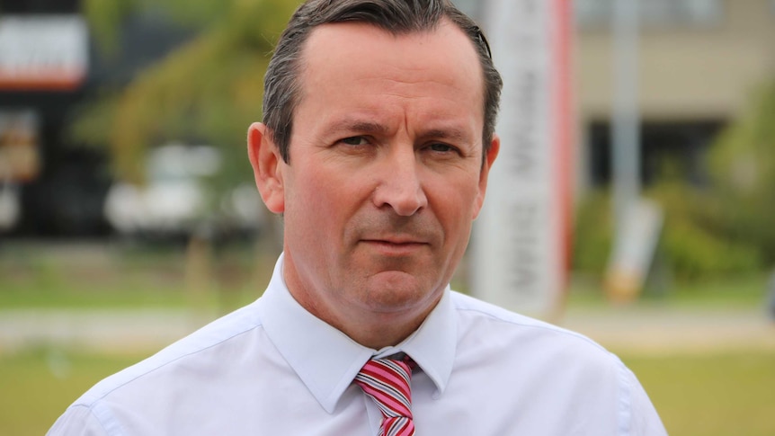 WA Labor Leader Mark McGowan looks down the barrel of the camera wearing a white business shirt and a red tie.