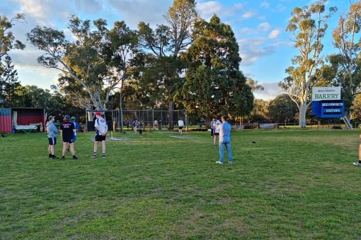 Un grupo de jóvenes observa a dos jugadores de cricket que practican en las redes de cricket.