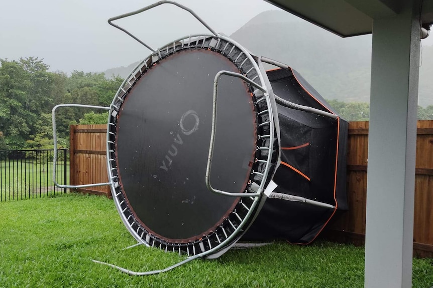 A trampoline is on its side against a fence.