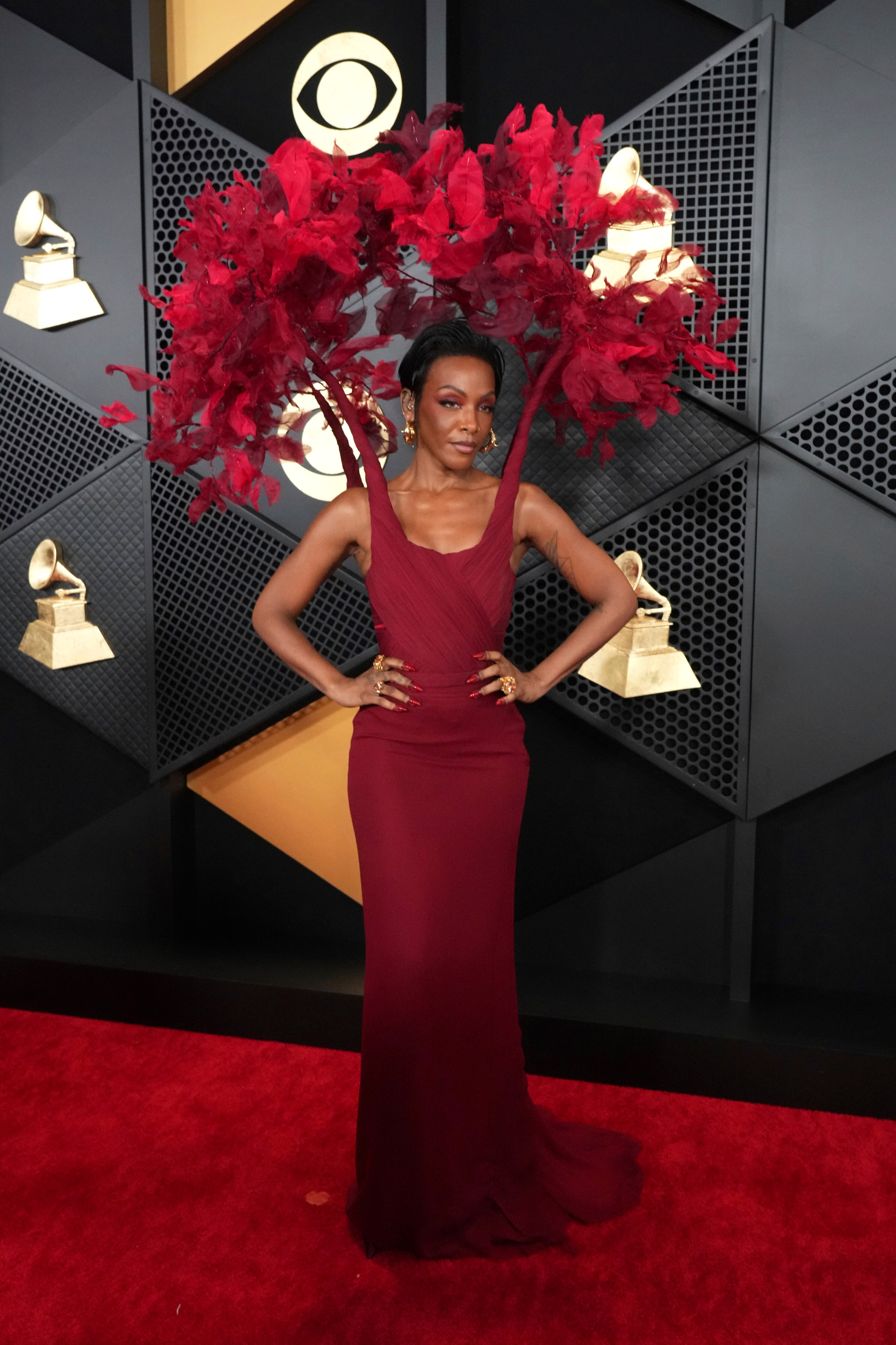 Dawn Richard wearing a fitted maroon dress with an attached headpiece with red feathers peacocking over her head