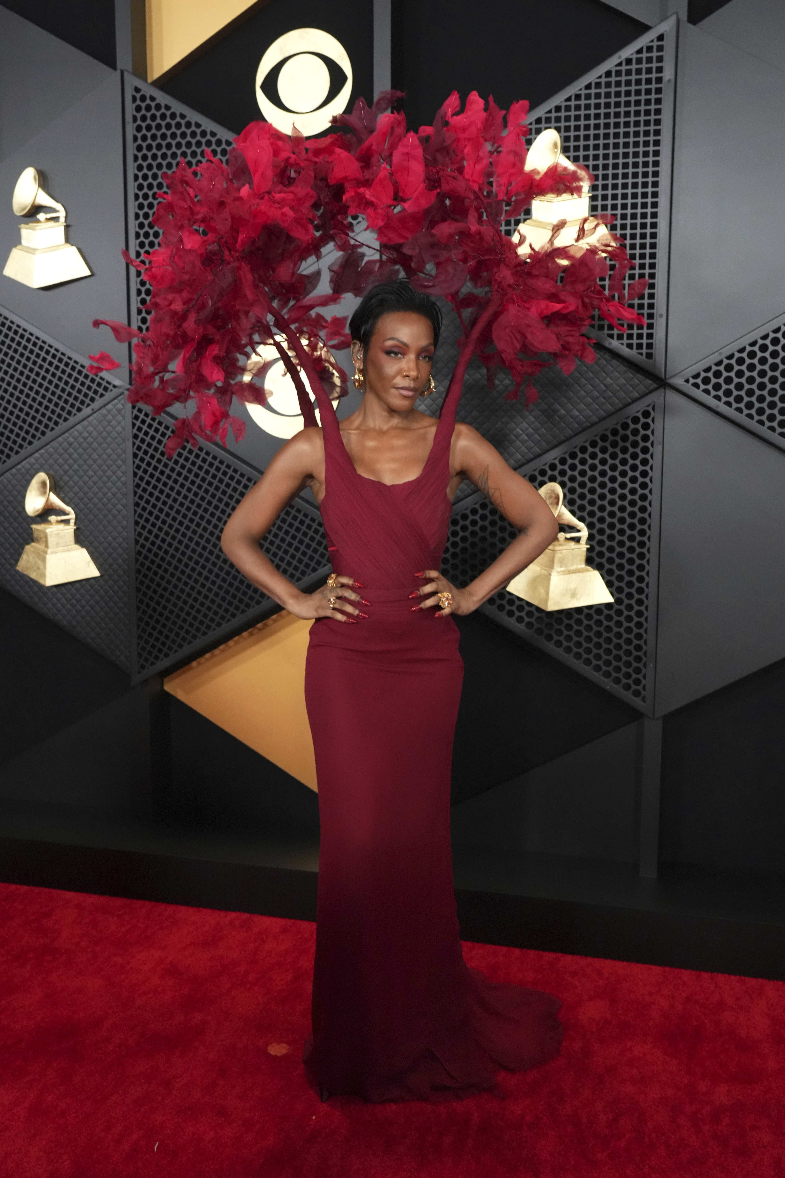 Dawn Richard wearing a fitted maroon dress with an attached headpiece with red feathers peacocking over her head