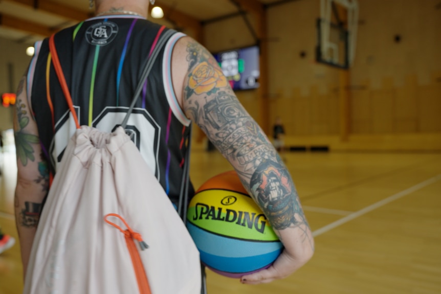 A QSA participant, with their back to the camera, holds a rainbow coloured basketball