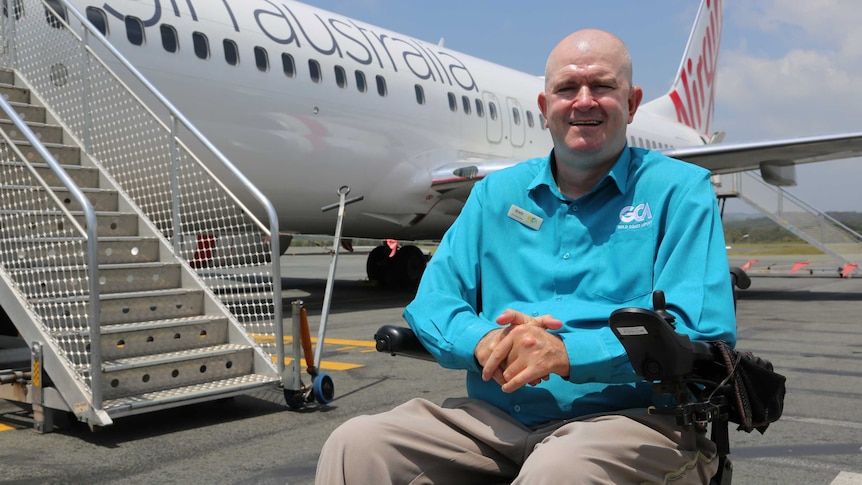 Brett Morris sits in a wheelchair on the tarmac in front of a Virgin Australia plane.