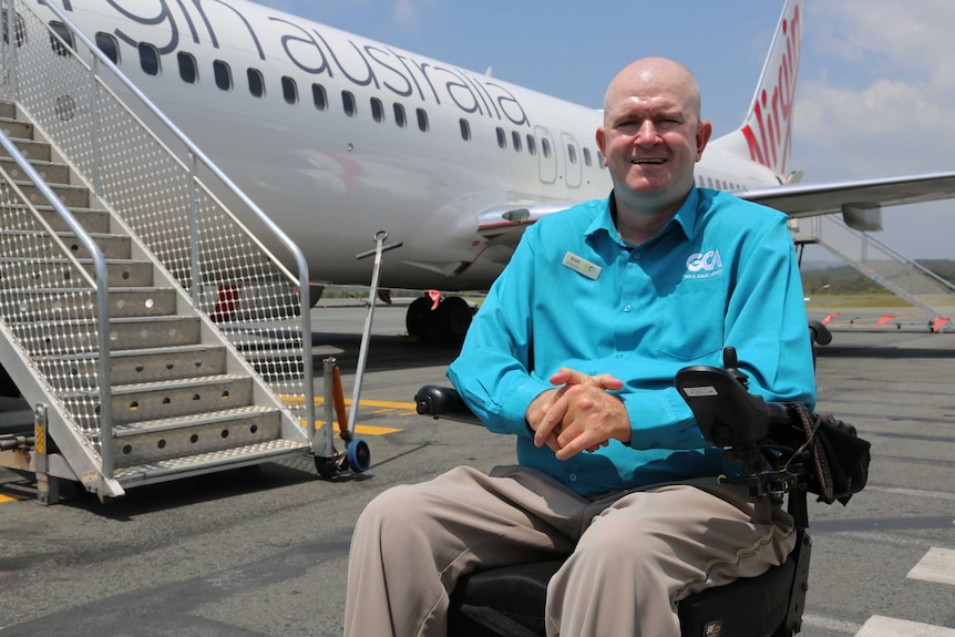 Brett Morris sits in a wheelchair on the tarmac in front of a Virgin Australia plane.