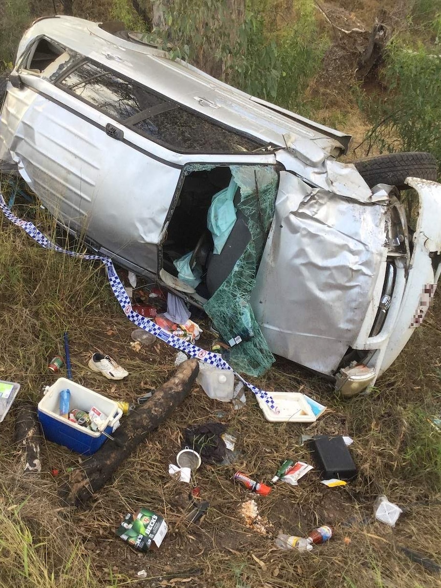 A silver four wheel drive on its side in the bush, badly damaged.