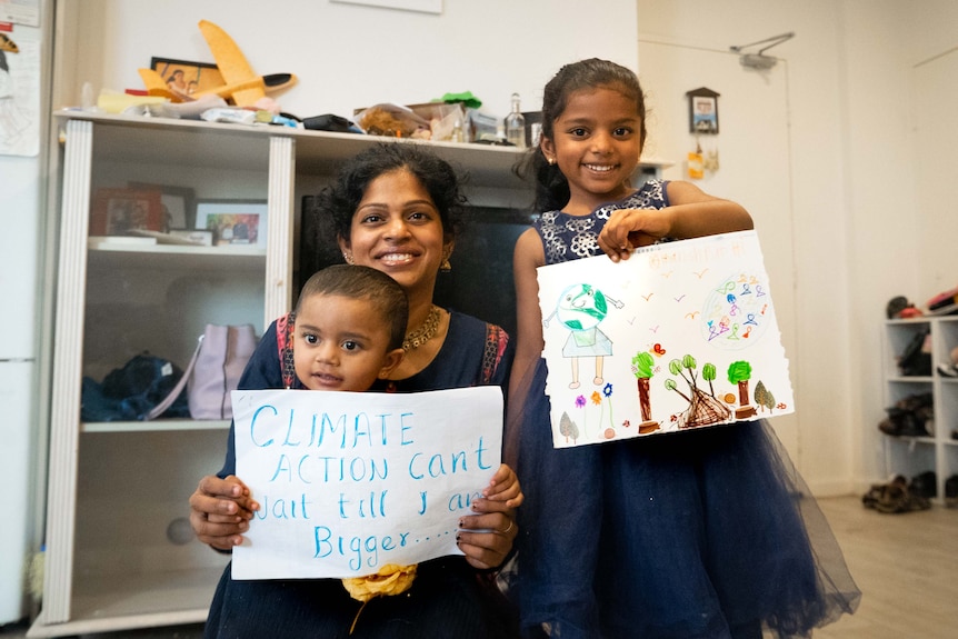 A woman and two young girls hold drawings. One says: climate change can't wait till I'm bigger.