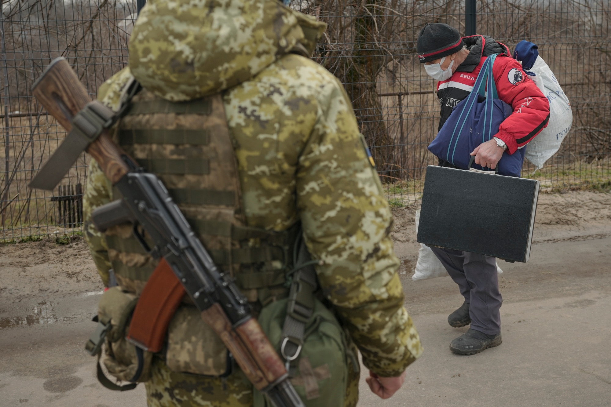 An elderly man holds his luggage as he crosses in front of pro-Russian separatists.
