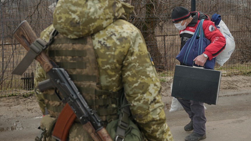 An elderly man holds his luggage as he crosses in front of pro-Russian separatists.