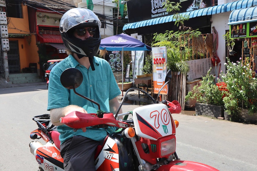A man wearing sunglasses wears a helmet while sitting idle on a red motorcycle
