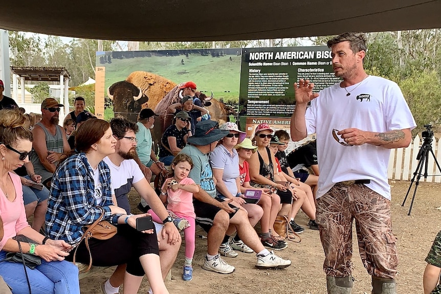 A man addresses a crowd of people at an animal park.