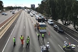 A line of vehicles backed up on the Mitchell Freeway with workers in hi vis gear in the foreground.
