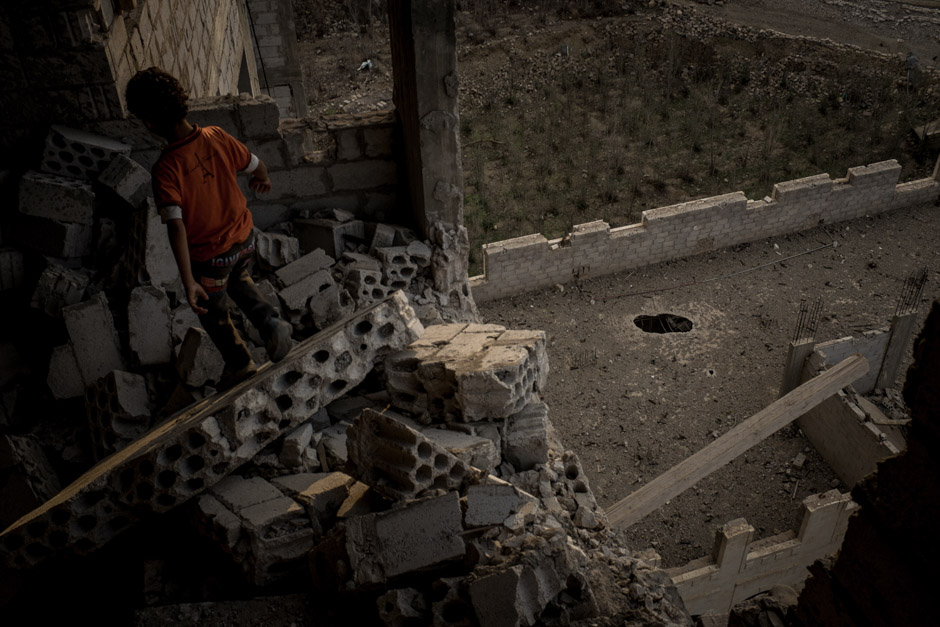 A young boy climbs through the rubble of a damaged apartment building.