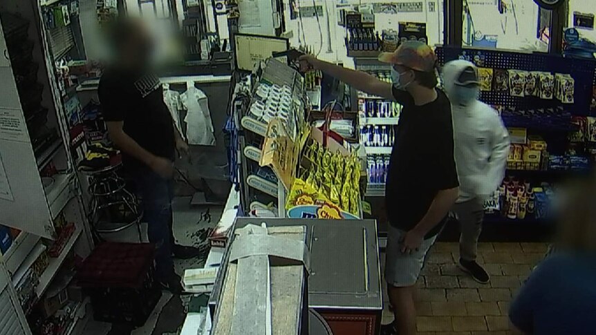 a man holding up a gun against a cashier in a grocery store