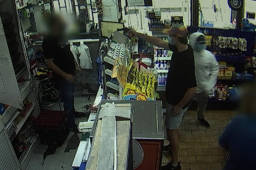 a man holding up a gun against a cashier in a grocery store