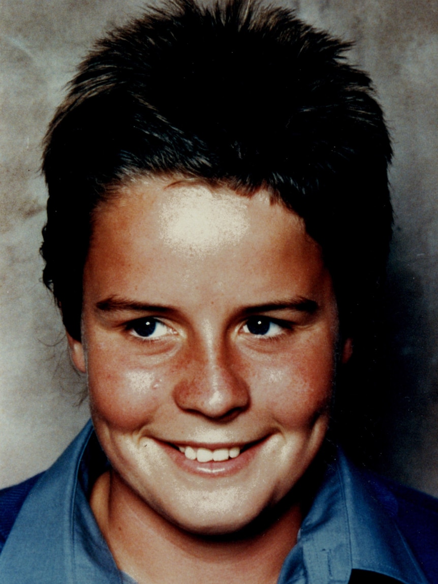 A picture of a smiling schoolboy wearing a blue shirt and blue top looking away from the camera.