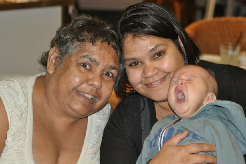 Two women holding a little yawning baby