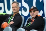 Justin Pascoe and Lee Hagipantelis sit on the sidelines at a Wests Tigers game.