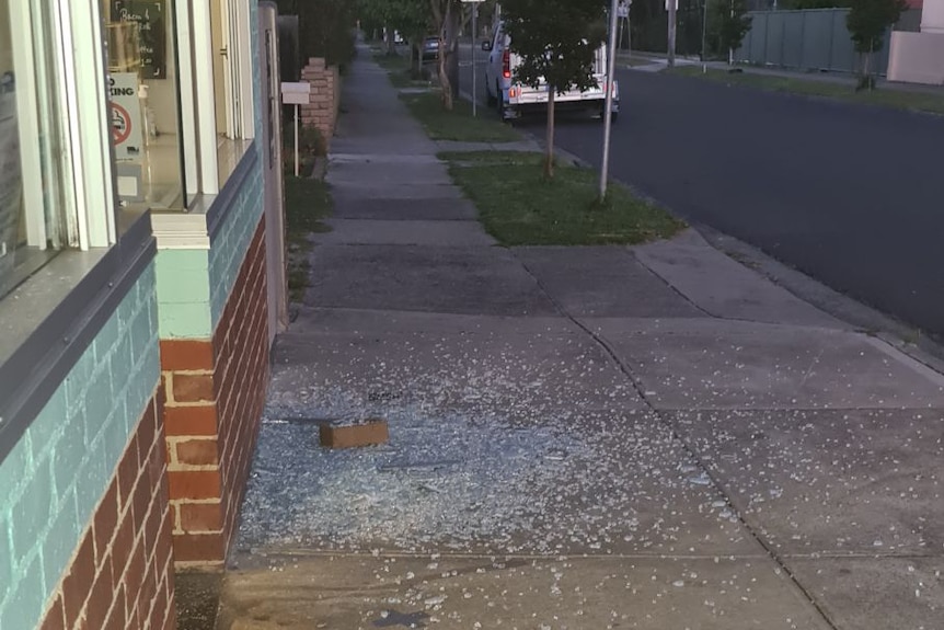 Shattered glass from a broken window litters a footpath.