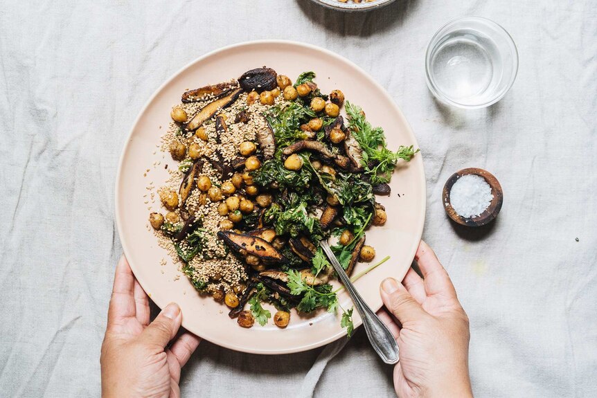 A pink plate of kale salad with pan fried shiitake mushrooms, crispy chickpeas and sesame seeds, a winter dinner.