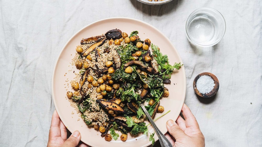 A pink plate of kale salad with pan fried shiitake mushrooms, crispy chickpeas and sesame seeds, a winter dinner.