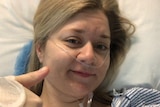 Katherine Goodall lays in a hospital bed while giving a thumbs up