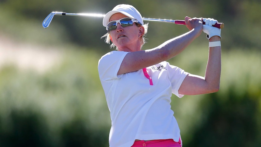 A female gofer in a white polo shirt with red trim and red shorts has just teed off and is looking into the distance.