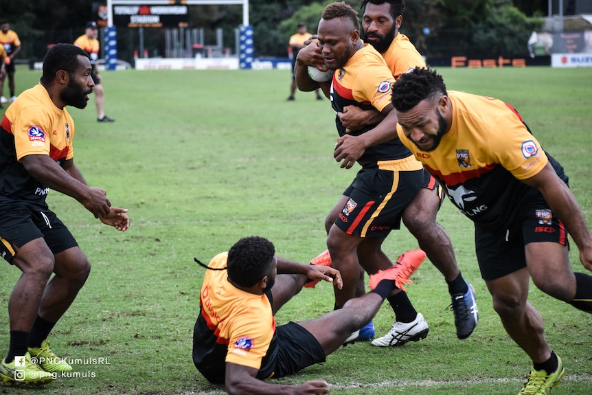 A PNG rugby league team does a training drill with one player on the ground and the ball-carrier tackled from behind.