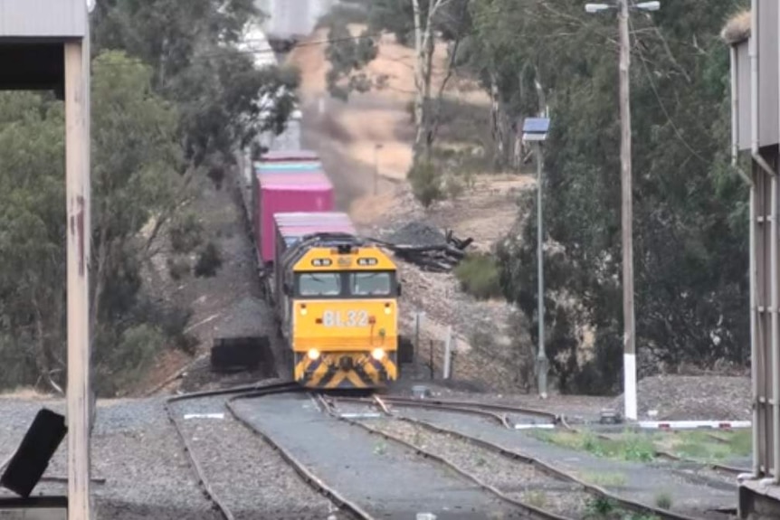 A freight train with a yellow engine, seen from the front, makes its way down a sloping section of track.