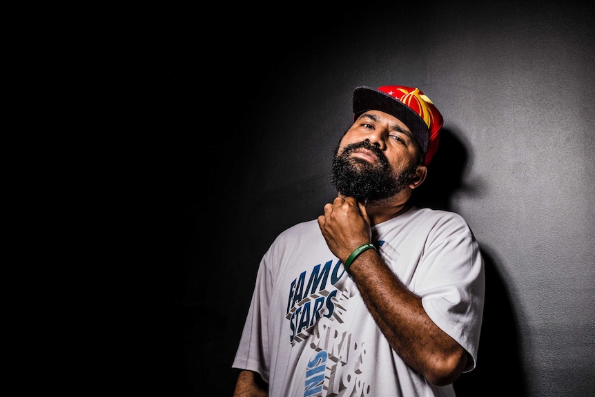 Mid-shot colour photograph of Port Moresby hip-hop artist MC Sprigga Mek leaning against a dark wall with a spotlight over him.