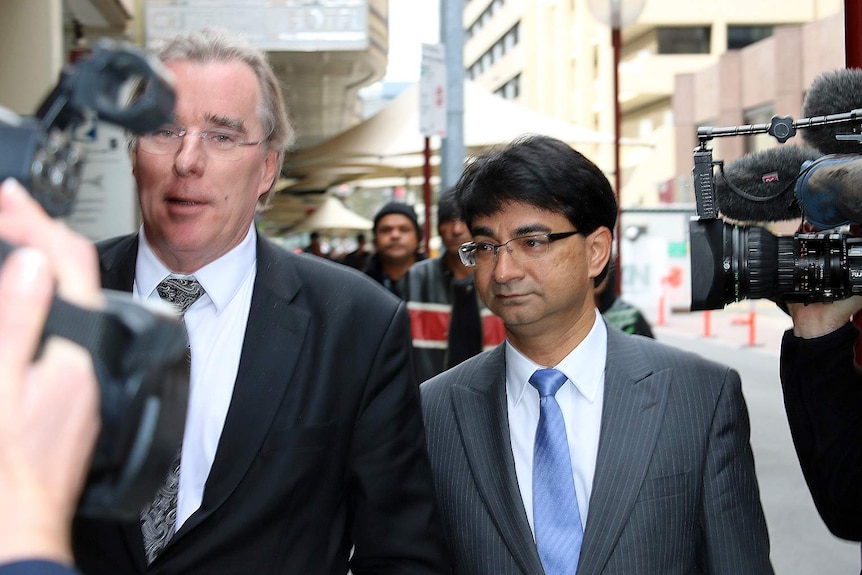 Lloyd Rayney walks along the street next to his lawyer and surrounded by TV cameras.