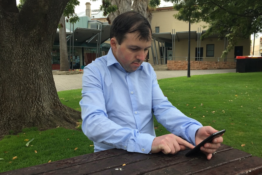 A man sitting at an outdoor table looking at a mobile phone