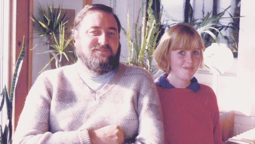 A photo from about the 1970s of a bearded man and young girl sitting in front of houseplants.