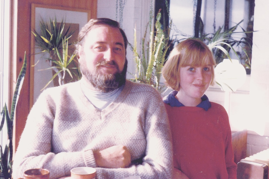 A photo from about the 1970s of a bearded man and young girl sitting in front of houseplants.