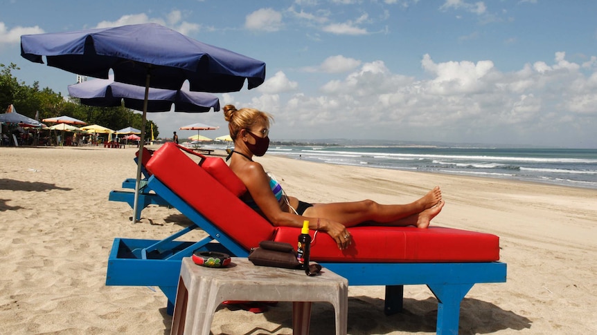 A female tourist wearing a protective face mask sunbathes on a beach in Bali.