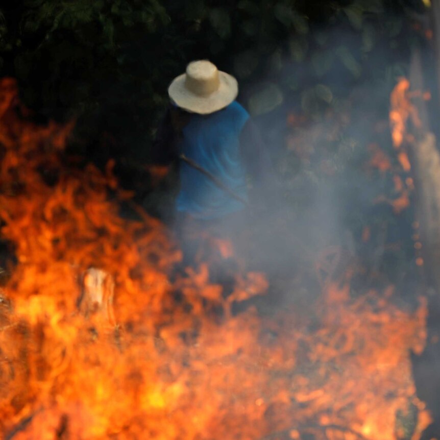 A man in a beige hat standing behind a fire.