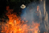 A man in a beige hat standing behind a fire.