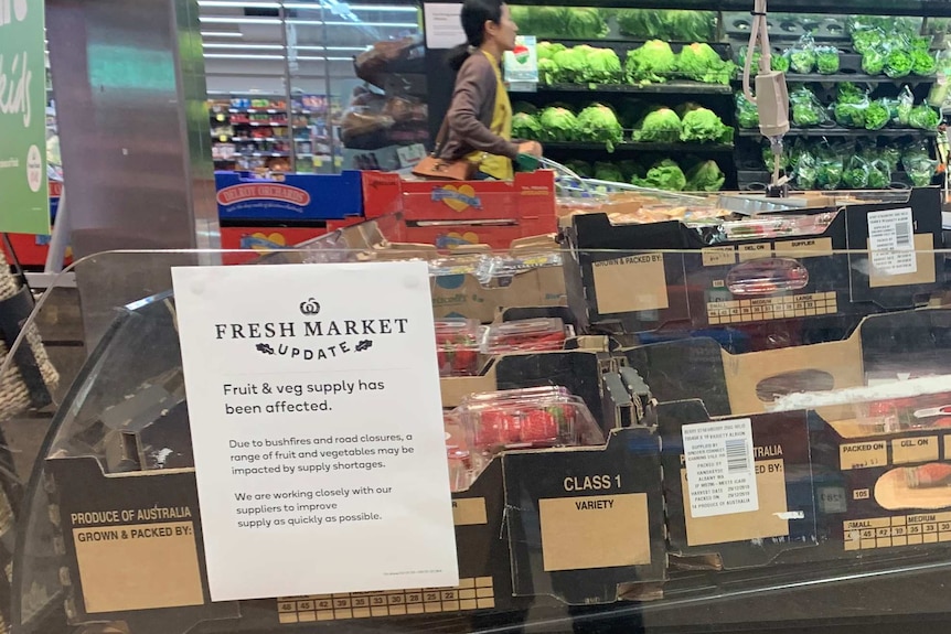 A sign in the fruit and veg section of a Woolworths store saying supplies have been affected by bushfires and road closures.