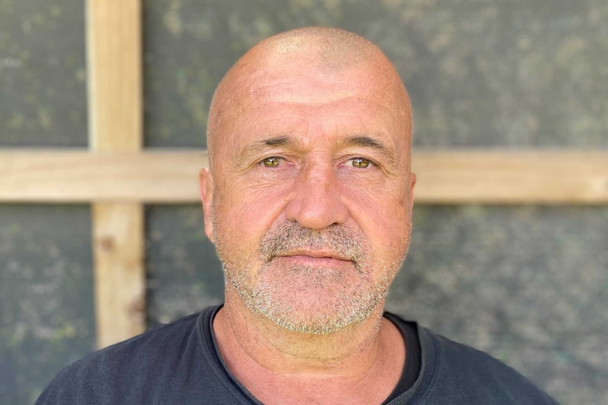 A man with a wrinkled face, glassy eyes and bald head looks straight into the camera.