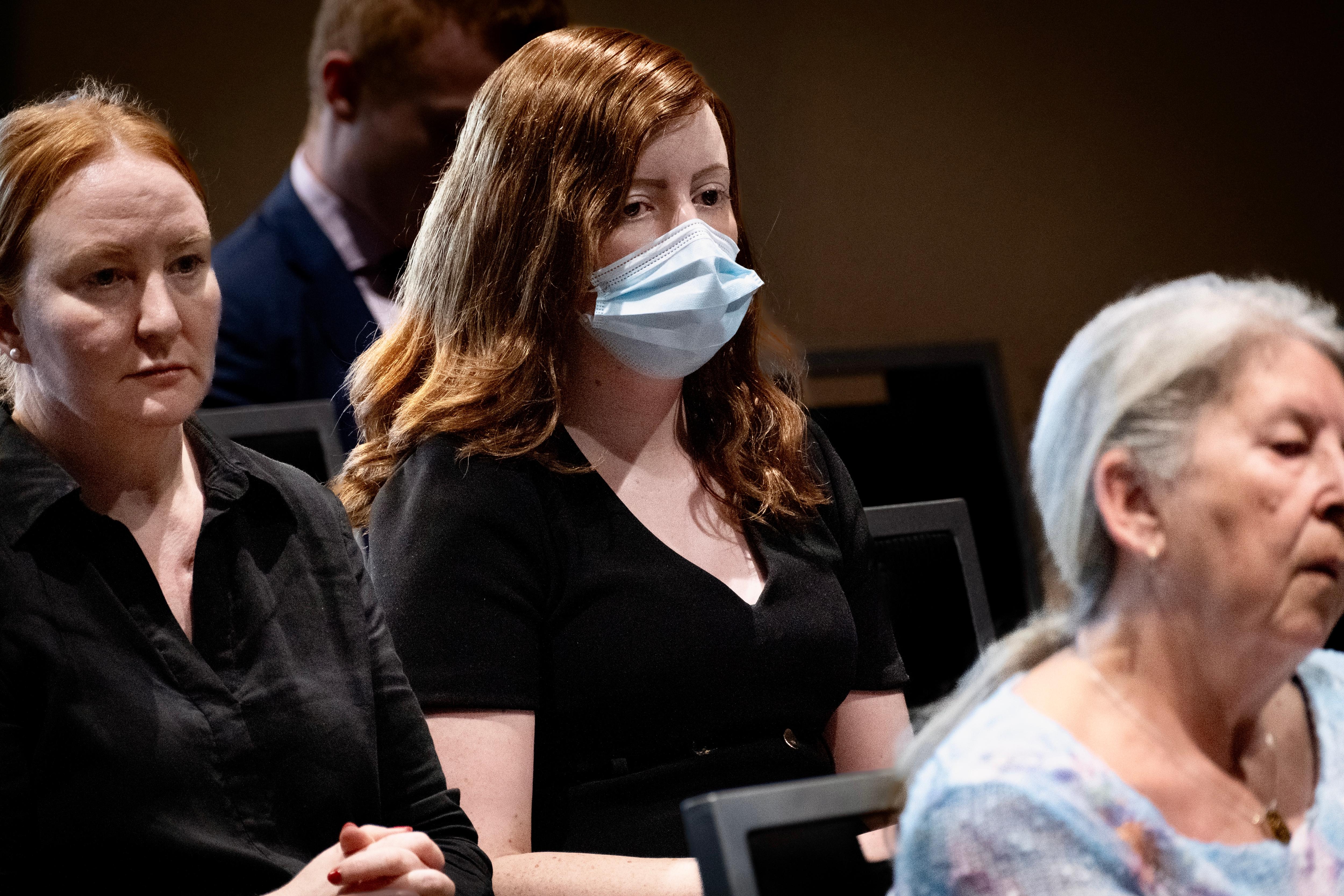 Katrina has red hair and wears a blue surgical face mask